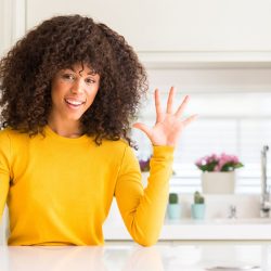 103729322 - african american woman wearing yellow sweater at kitchen showing and pointing up with fingers number ten while smiling confident and happy.